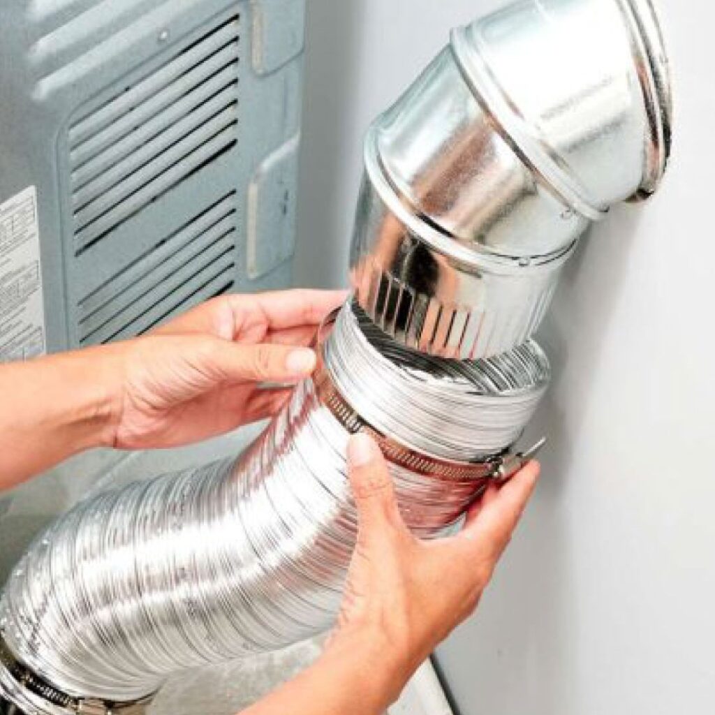 A technician installs a brand new silver metal dryer vent hose behind a dryer in a home. Environment is clean and white.